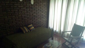 A room with a brick wall, a green sofa with striped pillows, a wooden chair, and a small table with magazines. - Posada Galicia (Villa Maria)