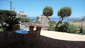 An outdoor patio with a round table and chairs, surrounded by brick flooring and greenery. - Elina Luxury Residence Villa (Chania)