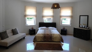 A bedroom with a bed, a sofa, a dresser, and a large window with blinds. - Elina Luxury Residence Villa (Chania)