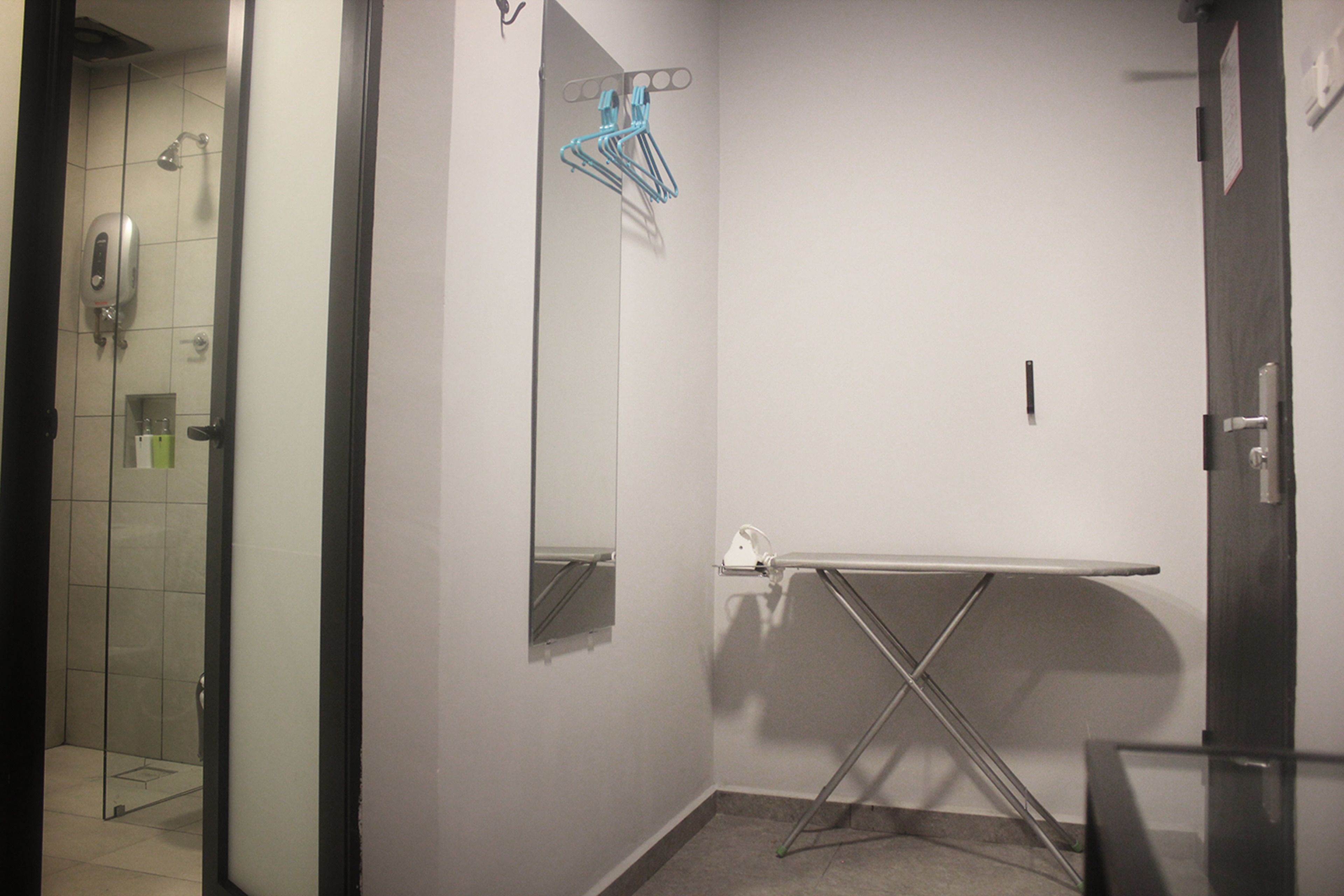 A hotel bathroom with a glass shower enclosure, a mirror, a towel rack, and a foldable ironing board.