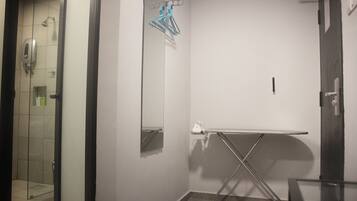 A hotel bathroom with a glass shower enclosure, a mirror, a towel rack, and a foldable ironing board.
