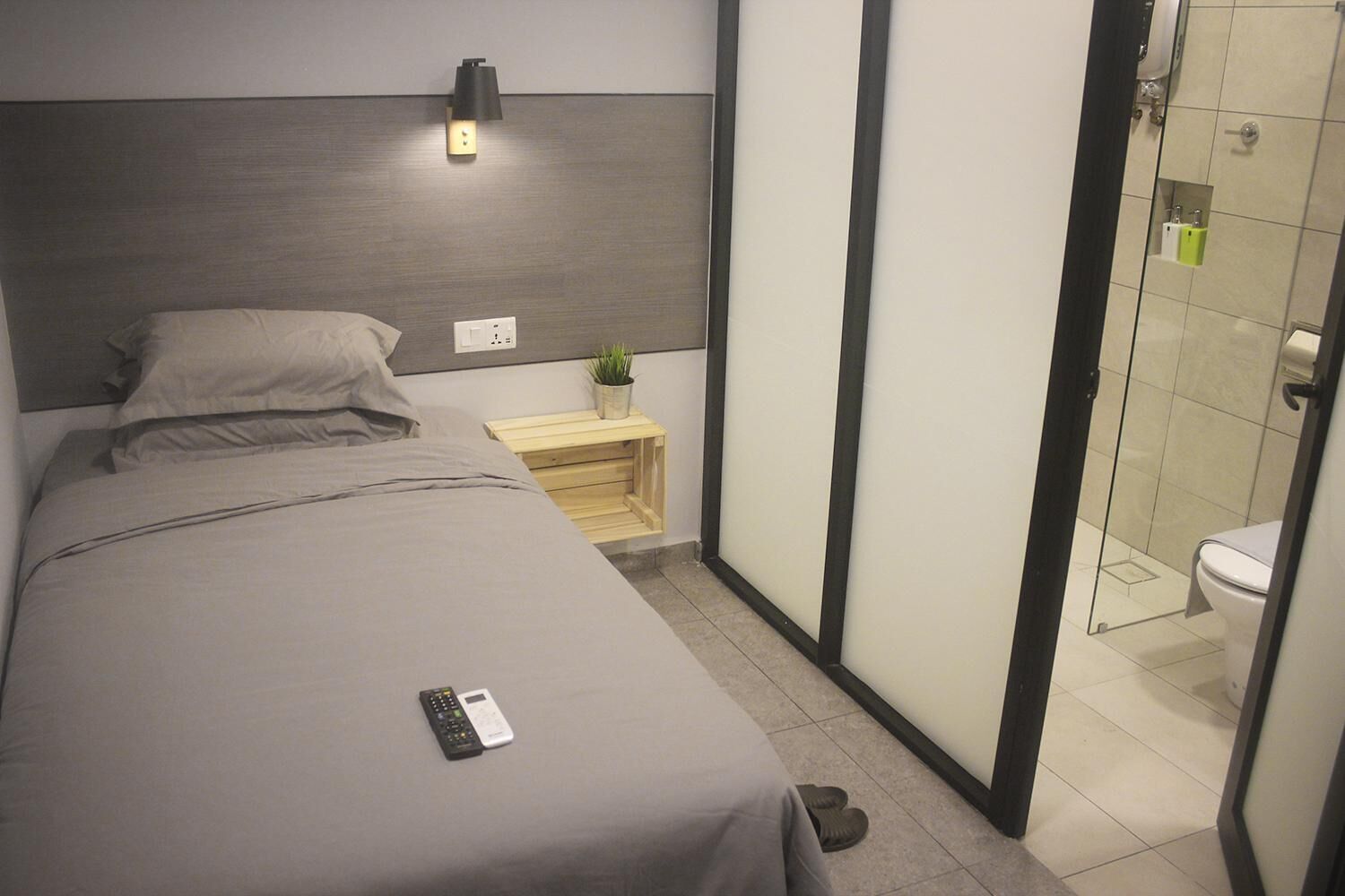 A hotel room with a bed, bedside table, lamp, and a view of the bathroom.