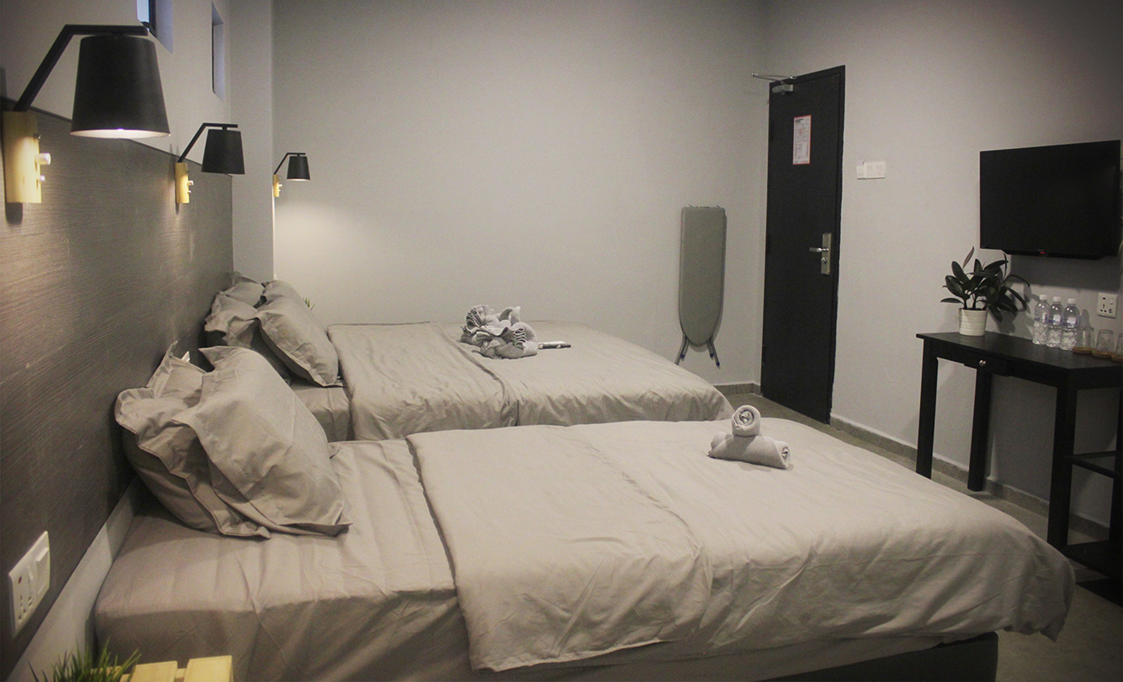 Ein Hotelzimmer mit zwei Betten, einem Schreibtisch mit Pflanze und Wasserflaschen, einem Wand-Fernseher und einer Tür.
