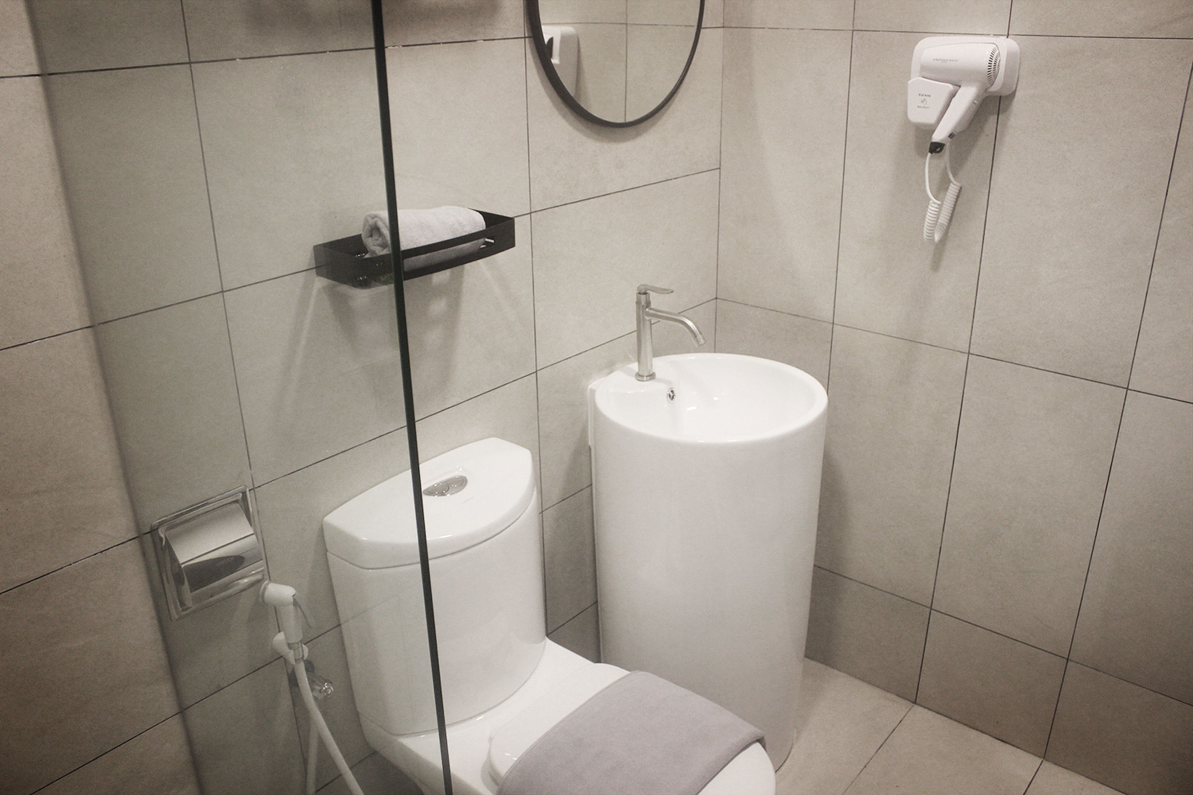 Un baño moderno con inodoro, lavamanos y un secador de pelo fijado a la pared.