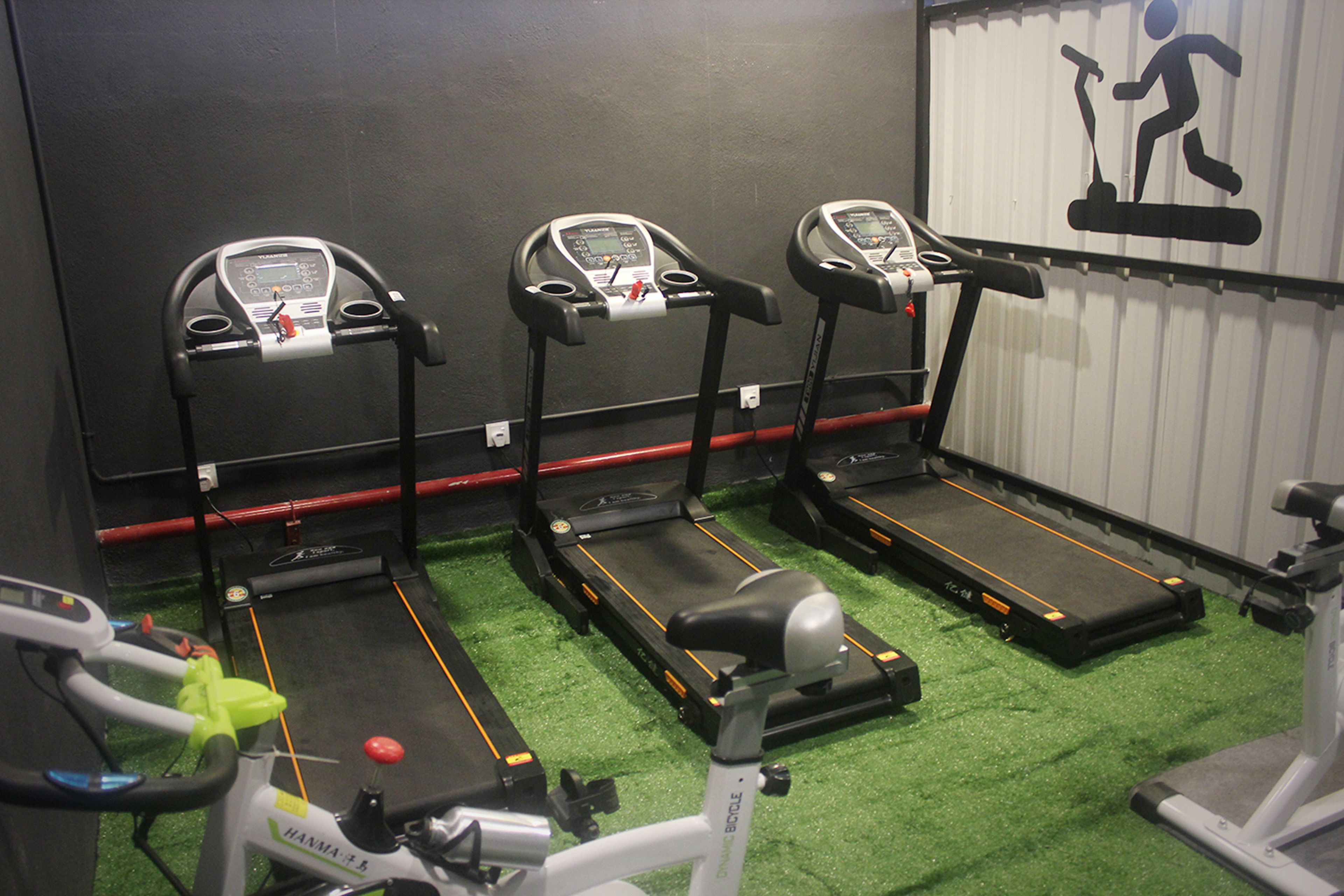 Three treadmills in a gym with green flooring and a wall-mounted exercise symbol.