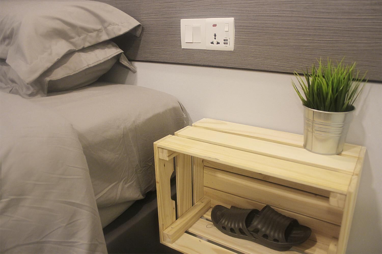 Un dormitorio con cama, una mesita de noche con una planta y un zapatero.