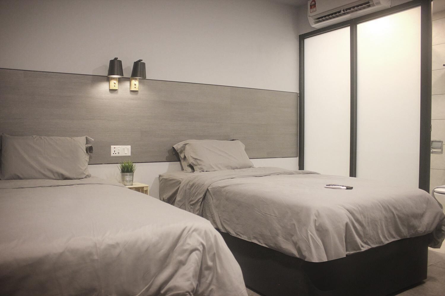 Habitación de hotel con dos camas, una mesita de noche con lámpara y un armario.