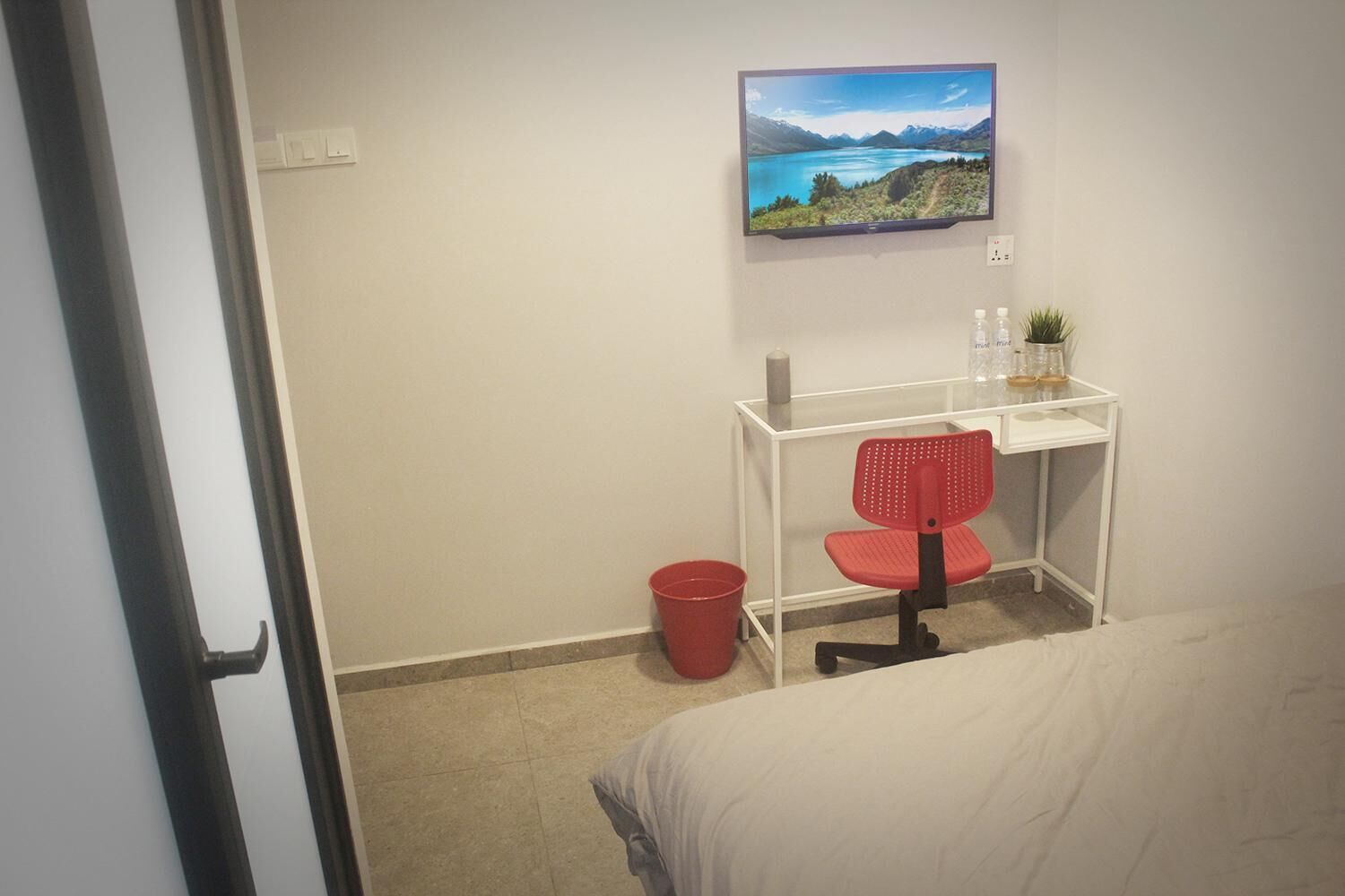 Een hotelkamer met een bed, een bureau met stoel, een televisie aan de muur en een kleine prullenbak.