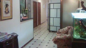 A hallway with a tiled floor, a framed picture on the wall, a desk with a lamp, and a fish tank. - Hostal Central (Zaragoza)