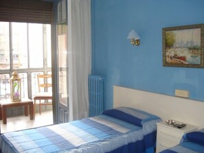 A bedroom with a bed, a chair, a table, a lamp, and a painting on the wall. - Hostal Central (Zaragoza)