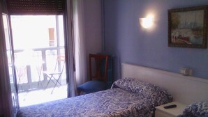 A room with two beds, a chair, a table, and a painting on the wall. - Hostal Central (Zaragoza)