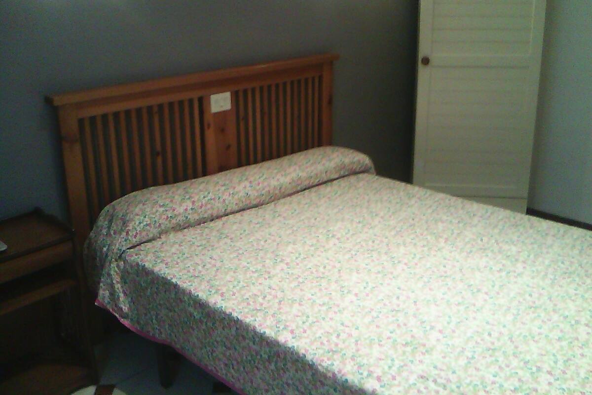 A small, single-bed room with a wooden headboard, a nightstand, and a door.