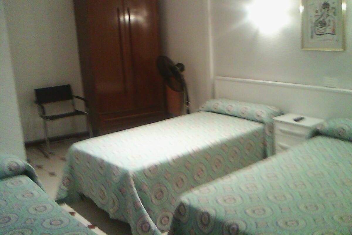 A bedroom with two single beds, a wardrobe, a chair, and a bedside table.