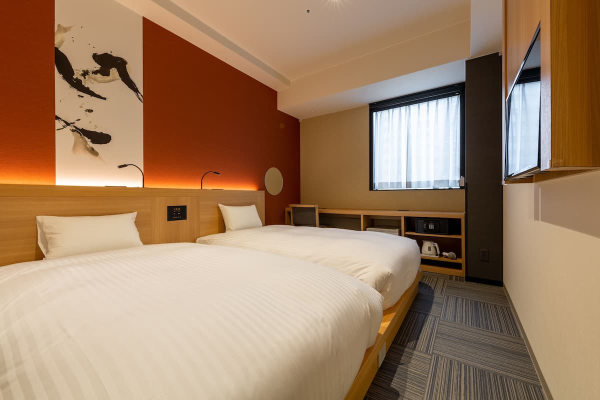 Une chambre d’hôtel avec deux lits, une télévision, un bureau et une fenêtre avec des rideaux.