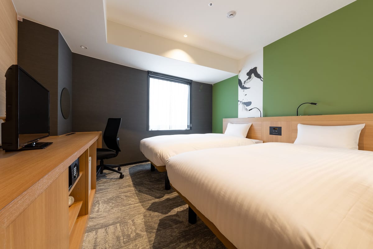 Une chambre d’hôtel avec deux lits, un bureau avec un ordinateur, une chaise et une grande fenêtre.