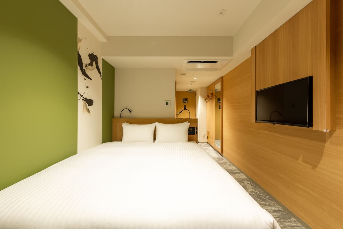 Une chambre d’hôtel moderne dotée d’un grand lit, de lambris en bois, d’un téléviseur à écran plat et d’un mur d’accent vert.