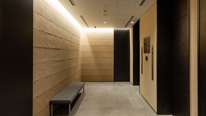 A modern elevator with a bench, a textured wall, and a dark door. - The OneFive Kyoto Shijo (Kyoto)