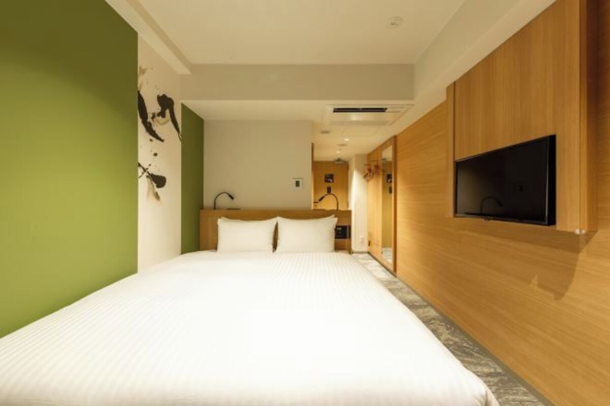 A hotel room with a large bed, wooden paneling, a flat-screen TV, and a green accent wall.