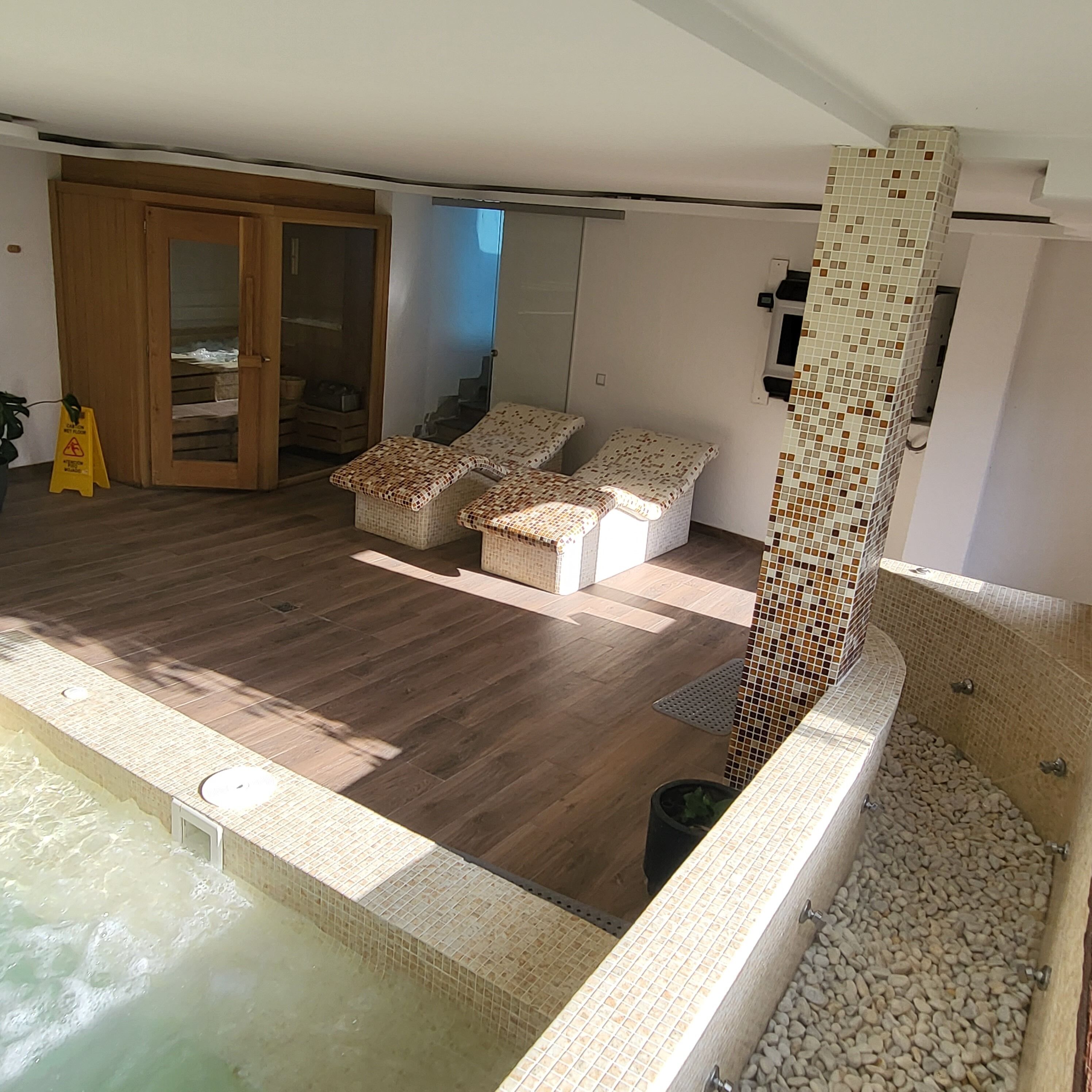 Un área de piscina interior amplia con suelo de madera, una zona de estar con bancos acolchados y un muro de azulejos.