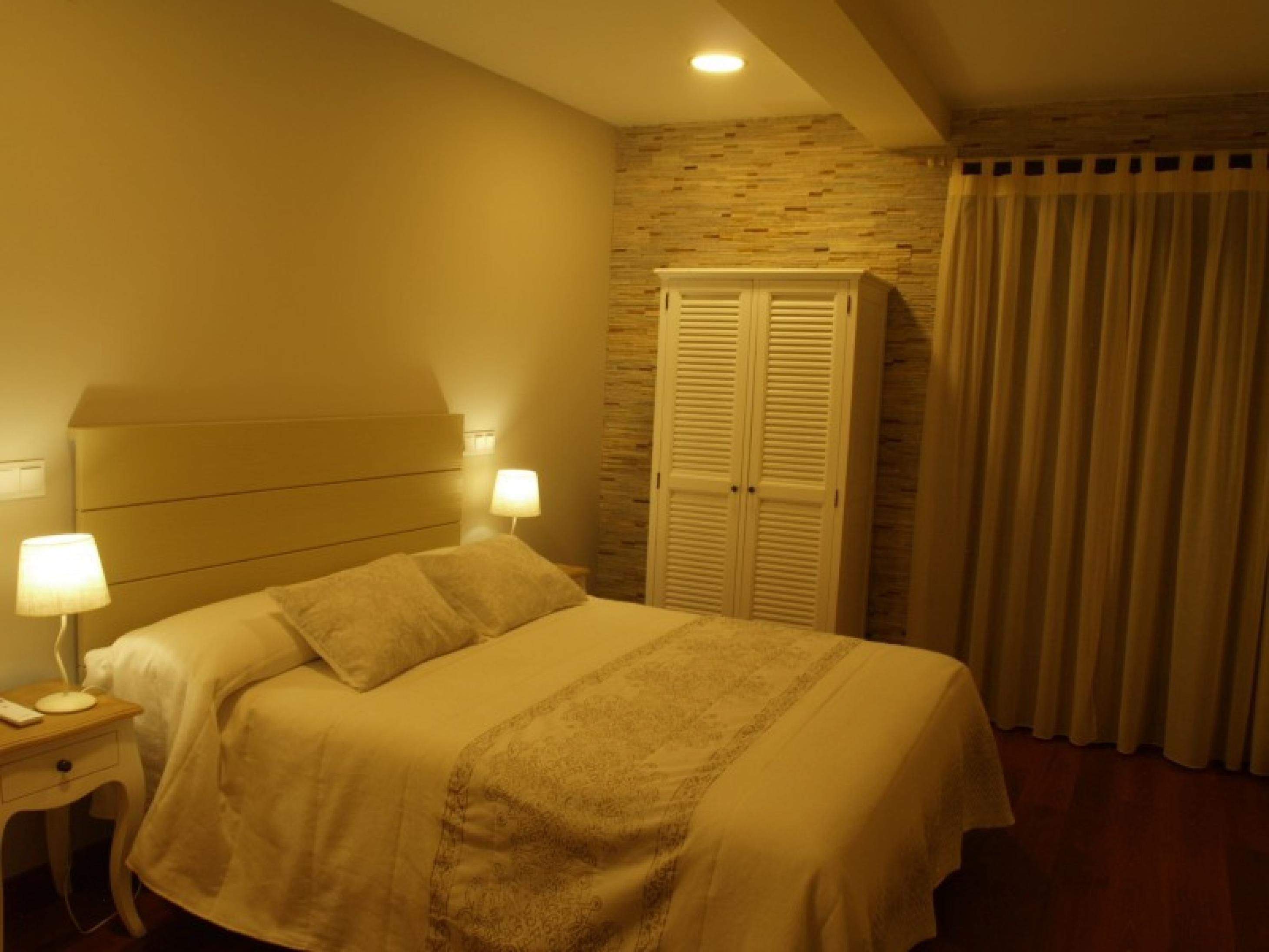 A hotel room with a bed, nightstands, a lamp, a wardrobe, and a curtain.