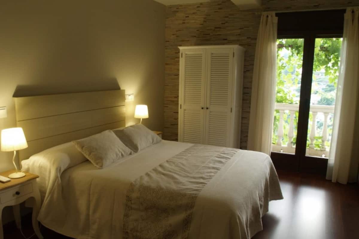 Quarto com cama, mesas de cabeceira, guarda-roupa e varanda com cortinas.
