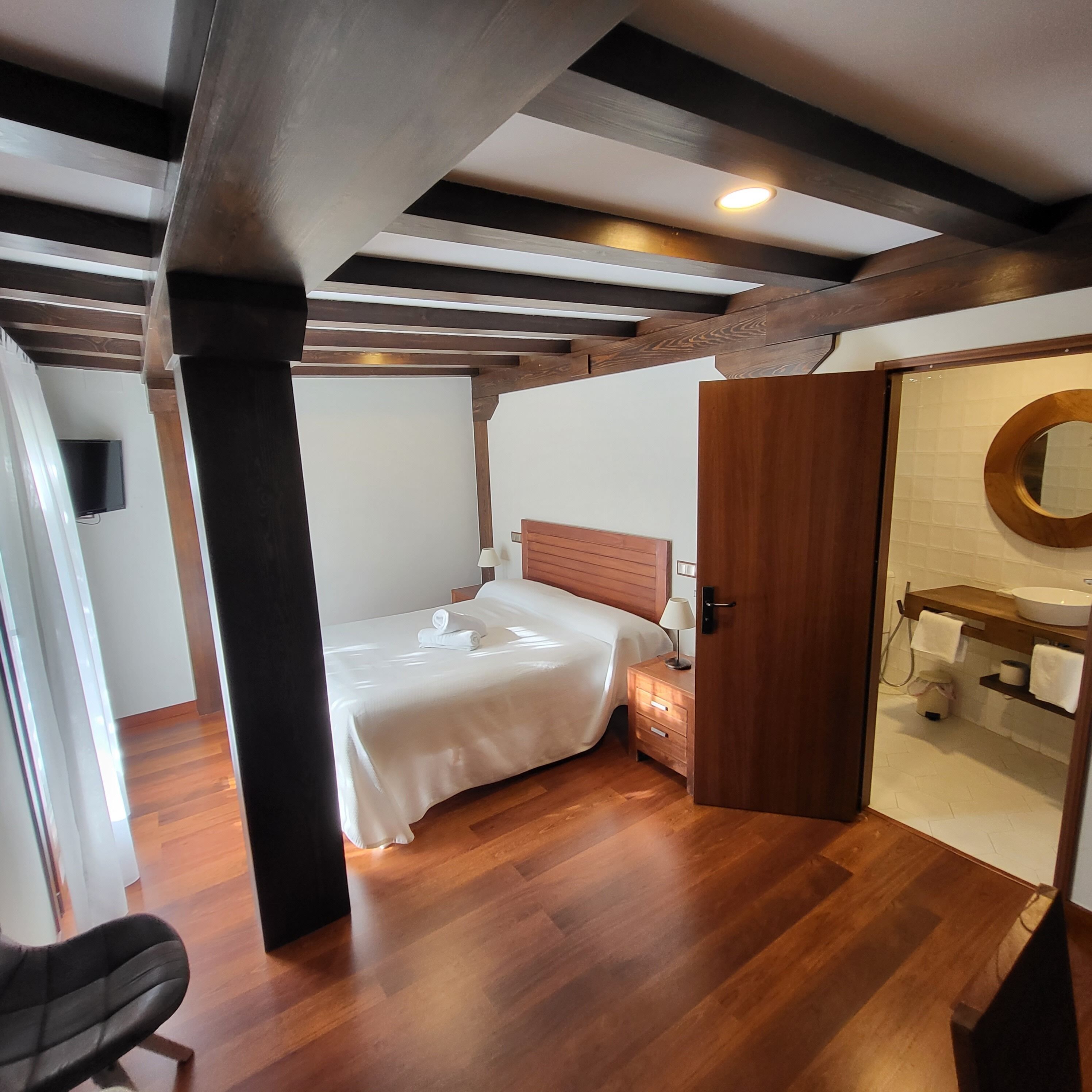 Une chambre à coucher avec un lit en bois, une table de chevet, un miroir et une salle de bain comprenant un lavabo et des toilettes.
