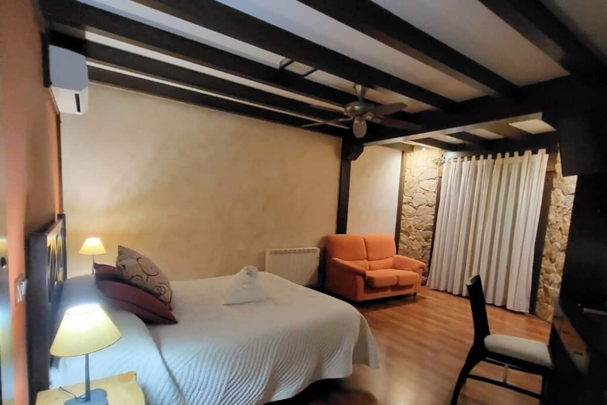 Quarto com cama, cadeira, abajur e ventilador de teto.
