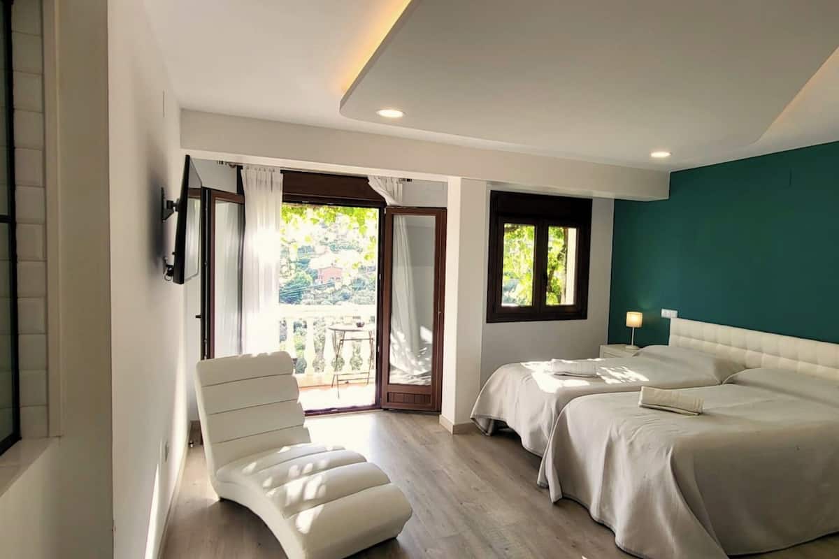 Quarto com duas camas, uma cadeira, televisão e varanda com cortinas.
