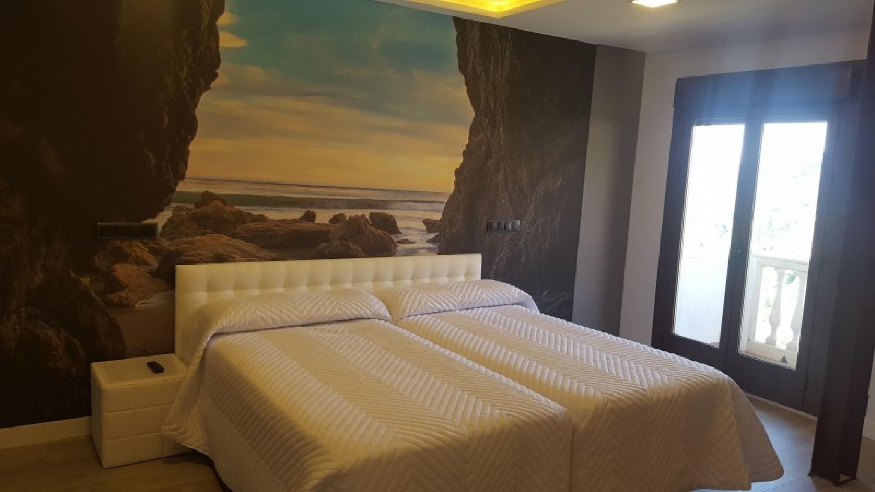 A bedroom with a large bed, a nightstand, and a view of the ocean through a window.