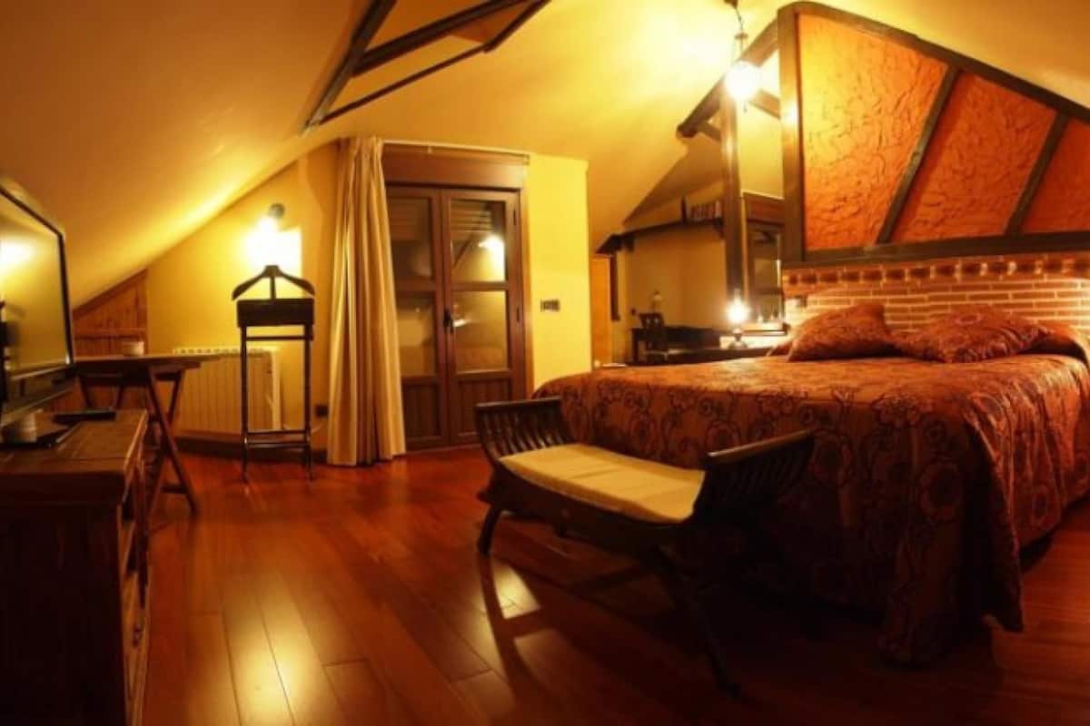 Um quarto de sótão aconchegante com teto inclinado, uma cama grande, uma escrivaninha e uma cadeira.