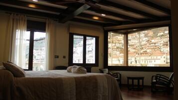 A hotel room with a bed, a window with a city view, a table, and two chairs.