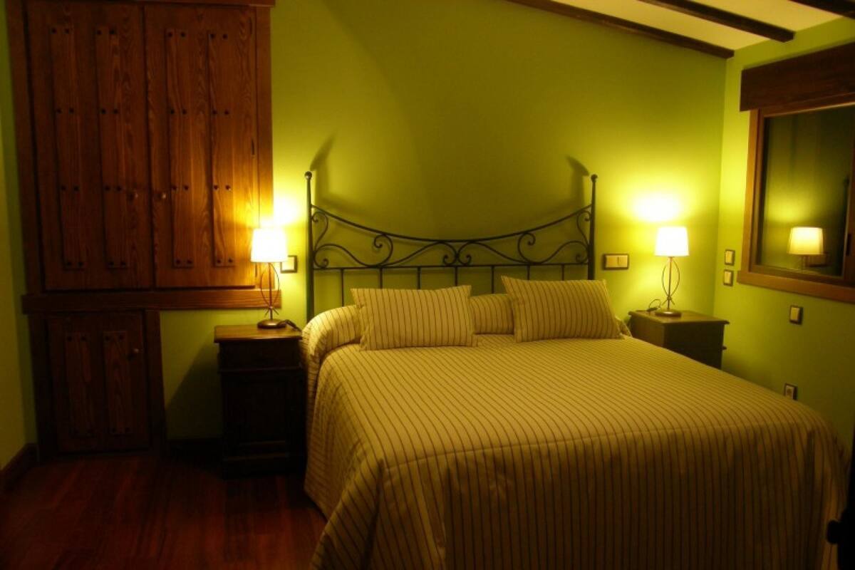 Quarto com cama, duas mesas de cabeceira, guarda-roupa de madeira e espelho na parede.