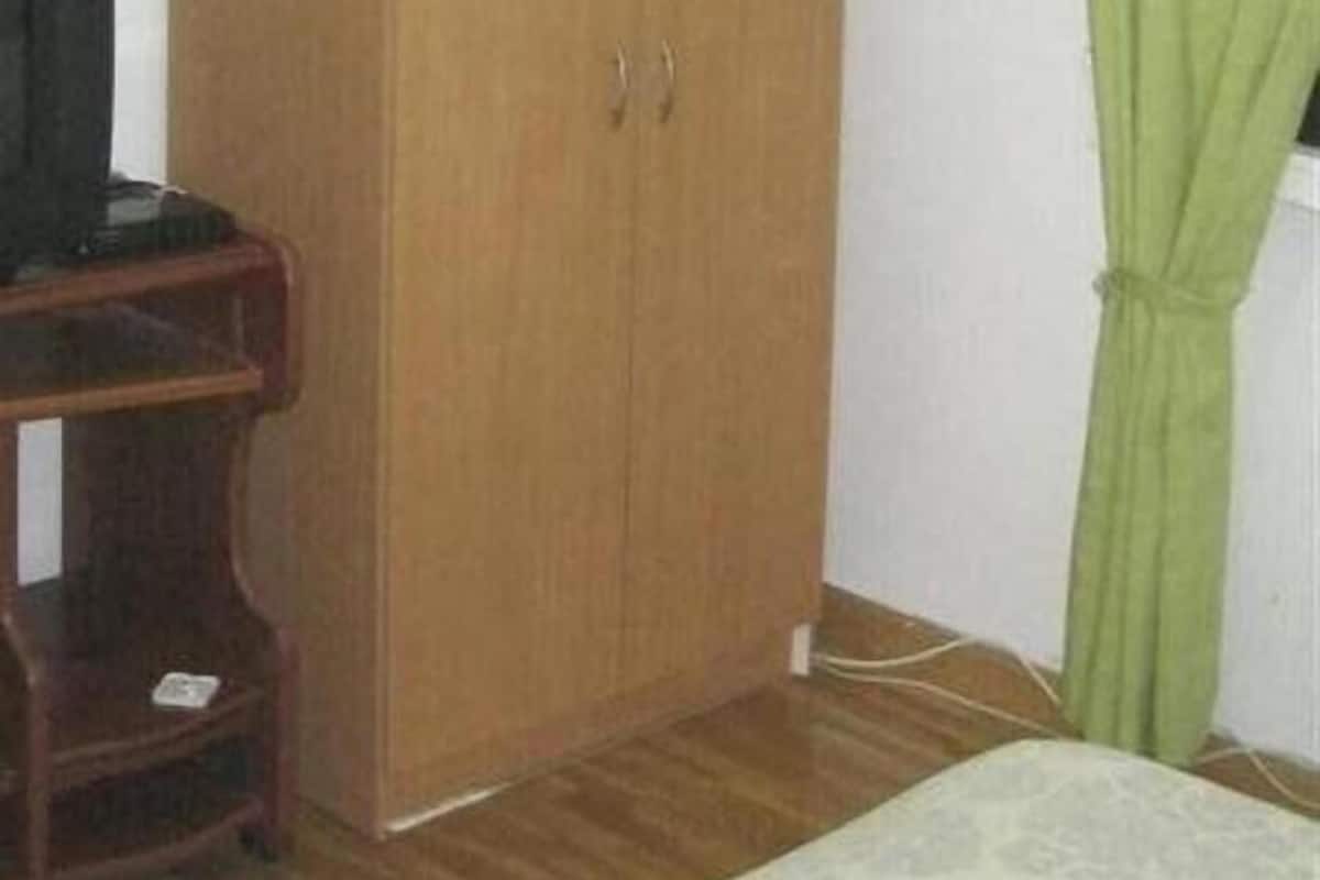 A room with a wooden wardrobe, a bed with a patterned bedspread, and a green curtain.
