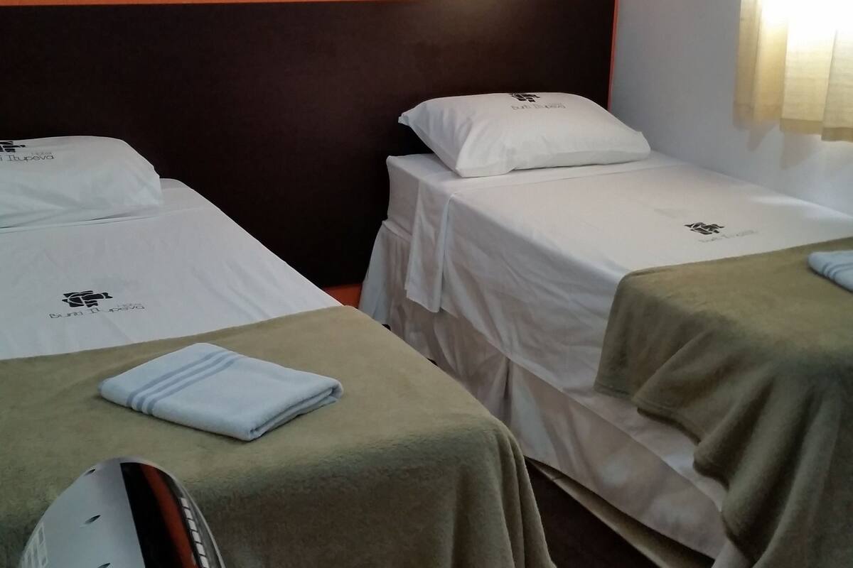 A hotel room with two single beds, a heater, and a small table.
