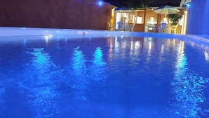 A swimming pool at night with blue lighting, surrounded by a building with outdoor seating and umbrellas. - Hotel Buriti Itupeva (Itupeva)