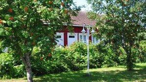 A red building with white trim, surrounded by lush greenery and trees bearing red fruits. - Opintola Bed & Breakfast (Teuva)