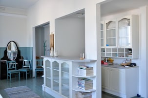 Um quarto com um piano, cadeiras, um armário branco com portas de vidro e uma estante de livros.