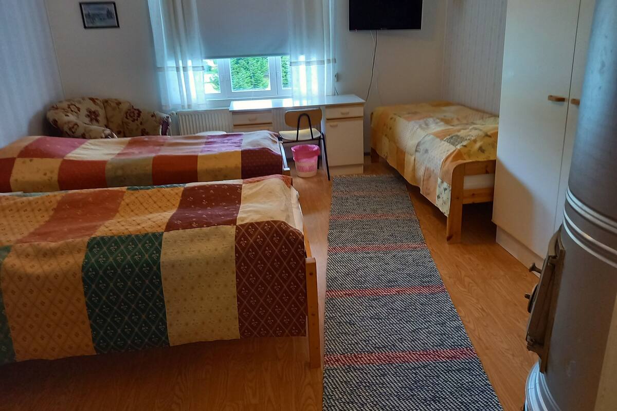 A room with two beds, a desk, a chair, a radiator, and a TV on the wall.