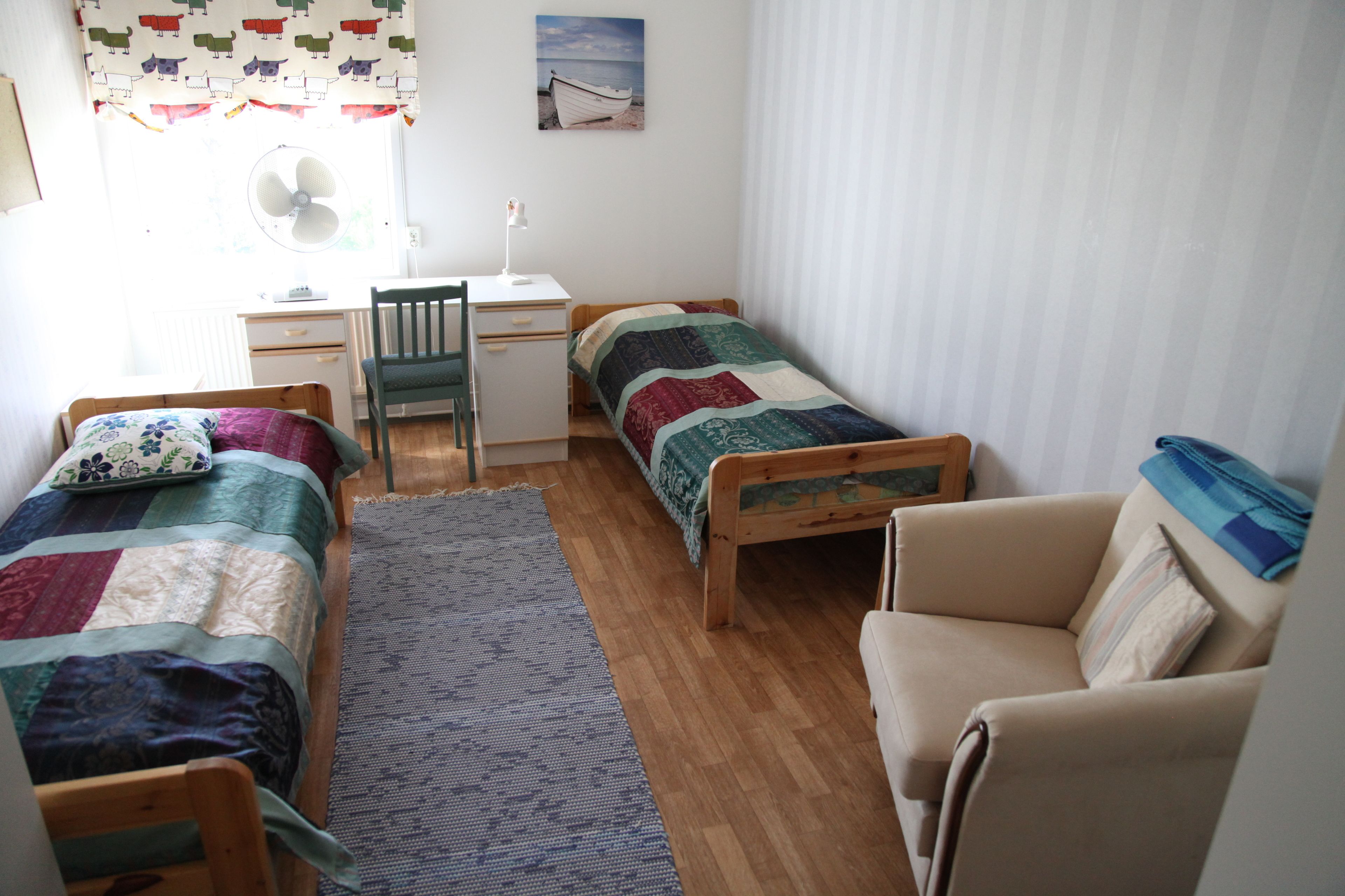 A small, tidy room with two single beds, a desk, a chair, and a sofa.
