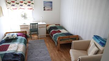 A small, tidy room with two single beds, a desk, a chair, and a sofa.