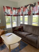 Uma sala de estar com um sofá marrom, uma mesa de centro de madeira e uma cortina florida.