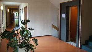 Een hotelgang met een potplant, een trap en een deur met een bordje.