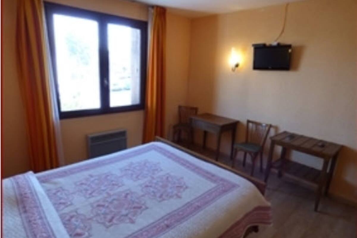 Een kamer met een bed, een bureau en een stoel. Er is een raam met gordijnen, een aan de muur bevestigde televisie en een radiator.