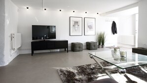 A modern living room with a glass coffee table, black sofa, grey ottomans, a black TV stand, and framed artwork on the wall. - WOW Apartments, Sankt Sigfridsgatan 64-66 (Gothenburg)