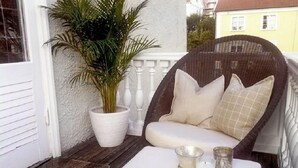 A wicker chair with cushions, a white table, and a potted plant on a porch. - WOW Apartments, Sankt Sigfridsgatan 64-66 (Gothenburg)