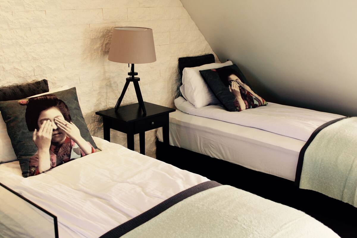 A bedroom with two beds, each with a pillow featuring a person's face. There is a nightstand with a lamp between the beds.