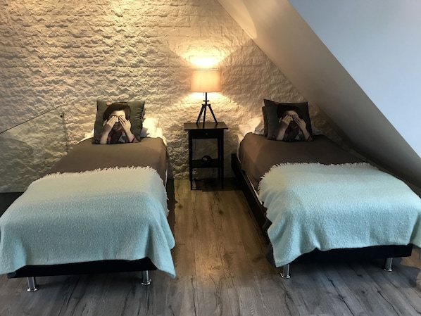 A cozy attic bedroom with two beds, a nightstand, and a lamp.