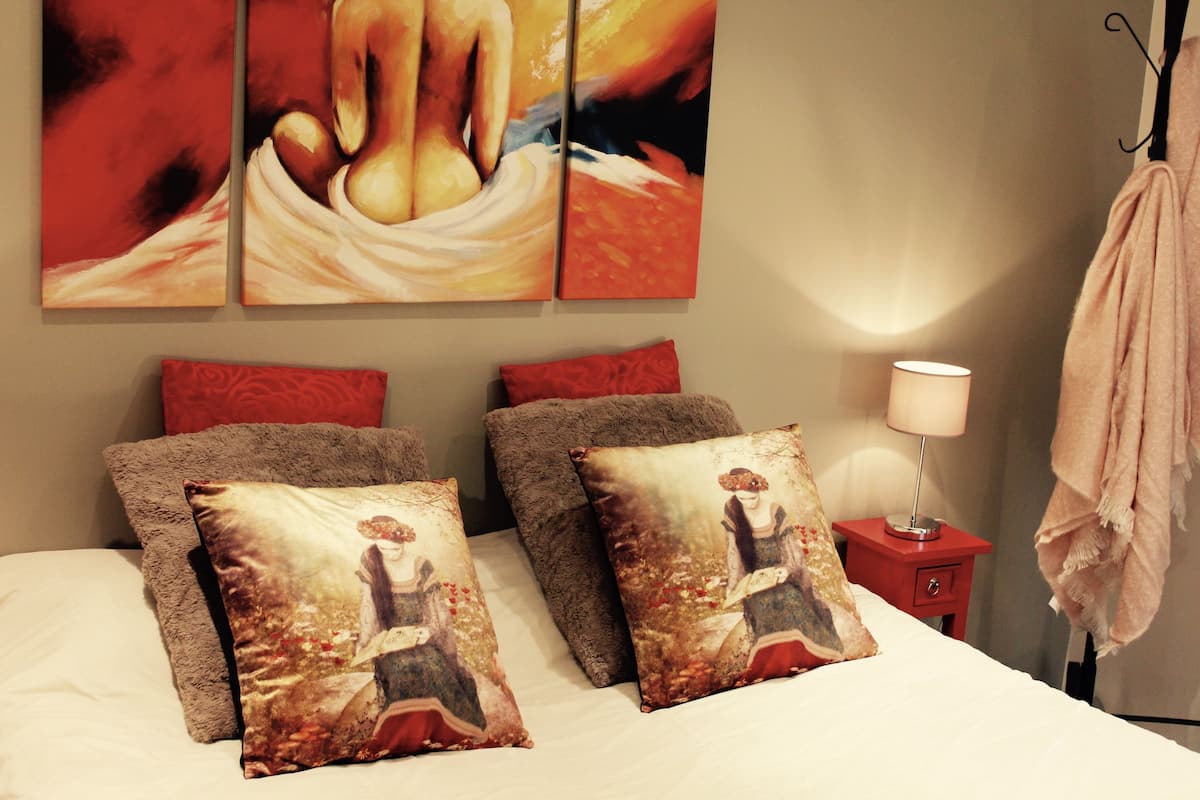 A bedroom with a bed, two pillows, a nightstand, a lamp, and a painting on the wall.
