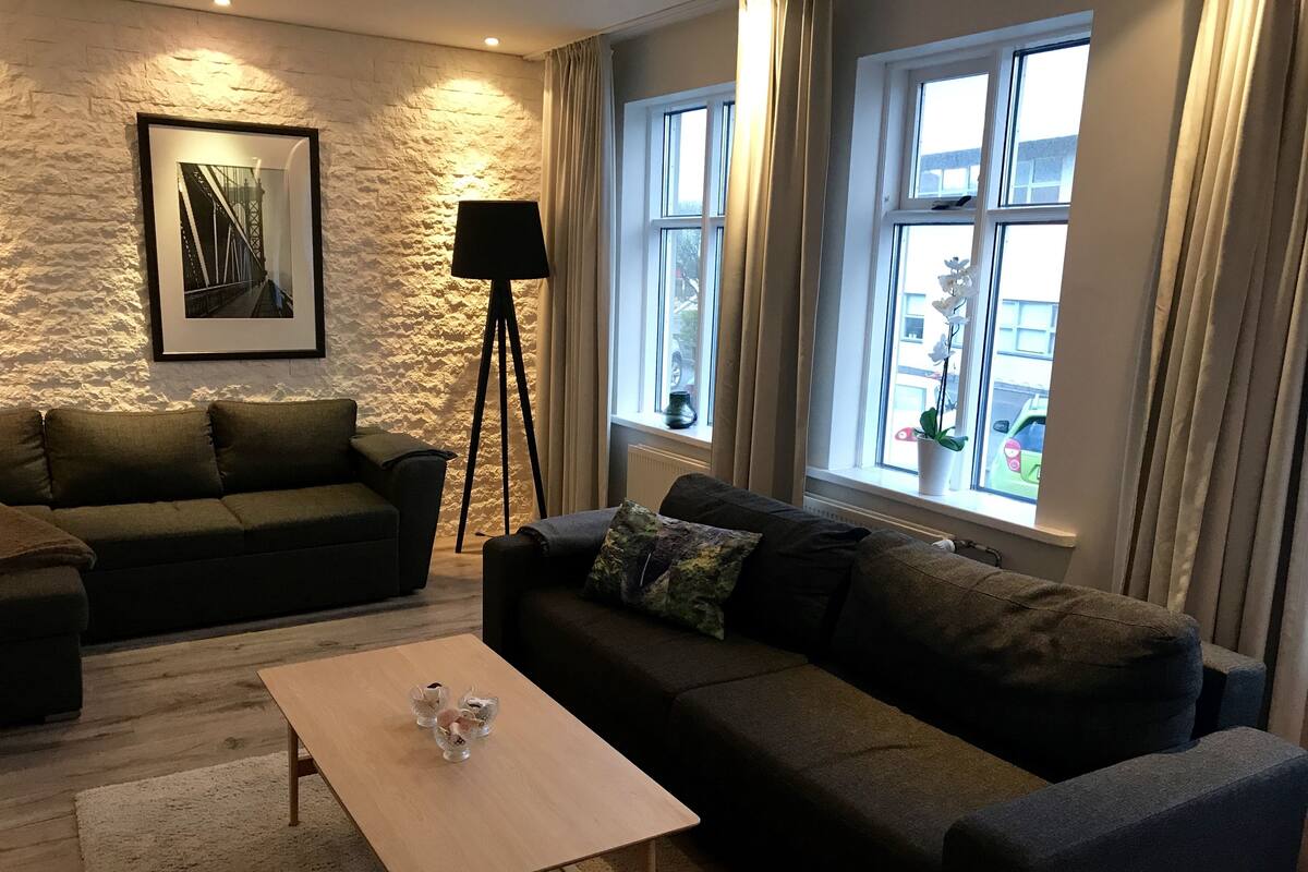 A modern living room with a stone accent wall, a framed picture, a floor lamp, and a view of the street through large windows.