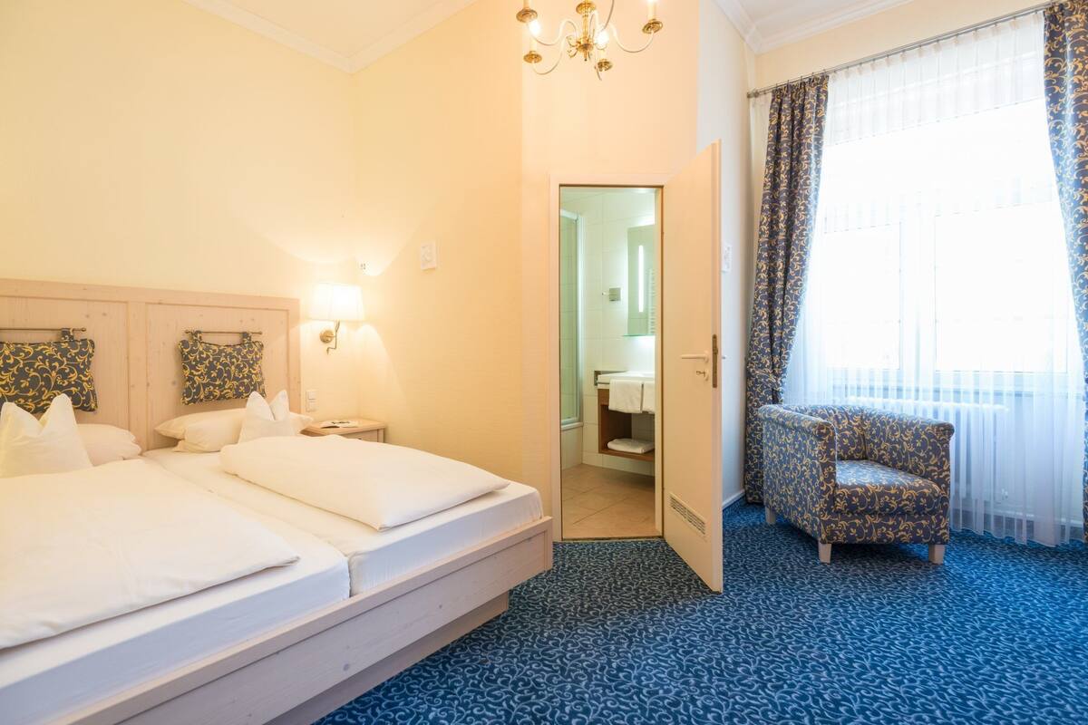 A hotel room with a large bed, a chair, a bathroom, and a view of the outside.